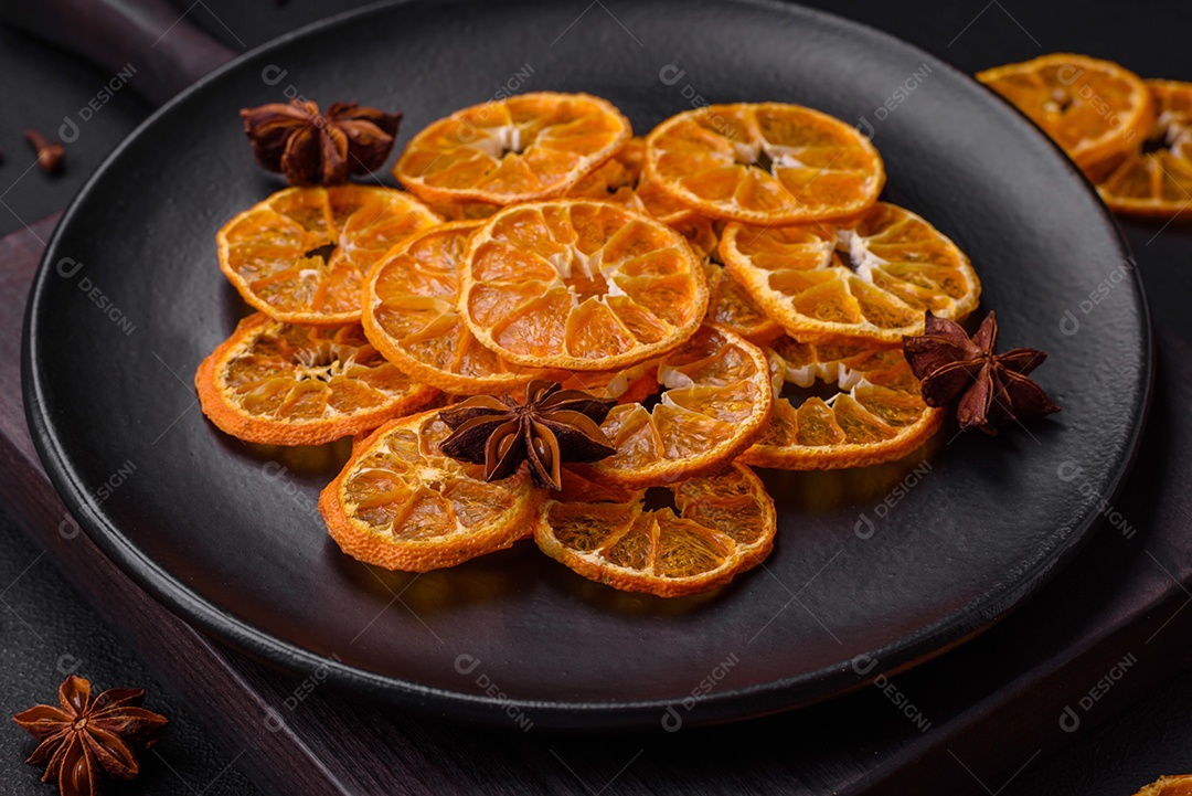 Fatias secas de forma redonda de tangerina de cor laranja brilhante sobre um fundo textural escuro