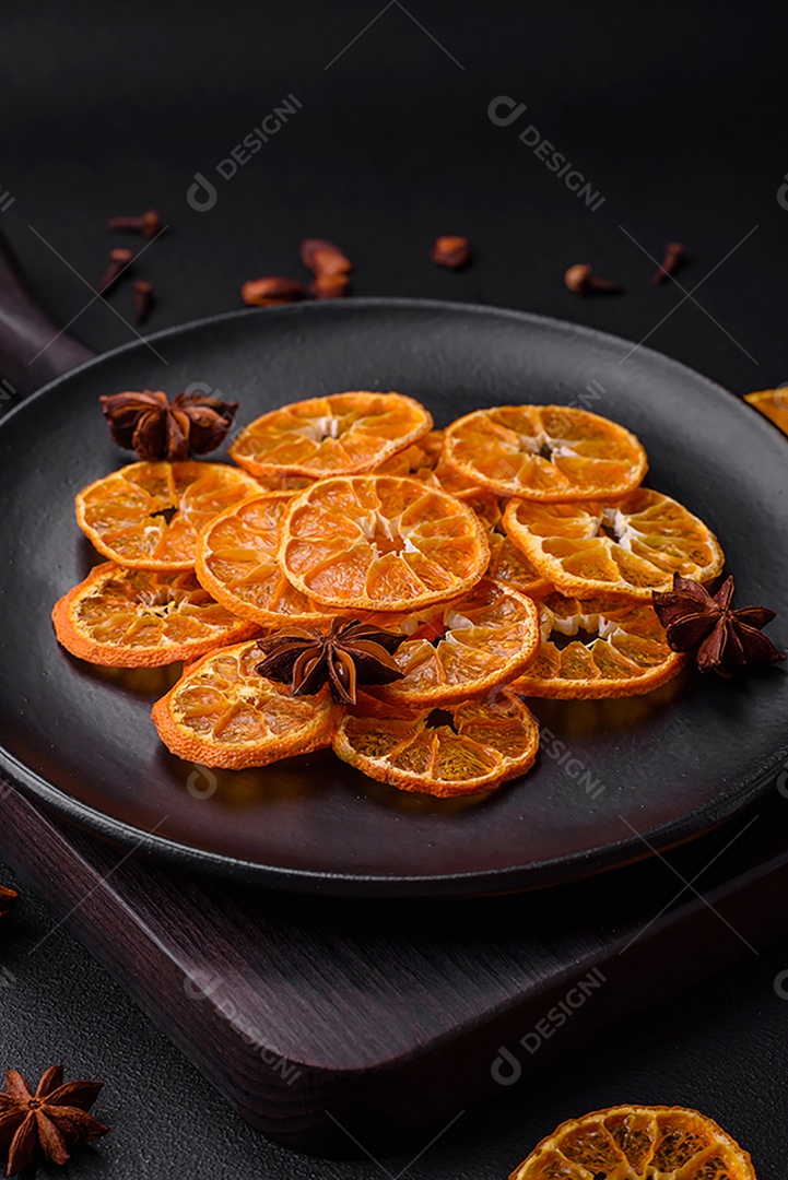 Fatias secas de forma redonda de tangerina de cor laranja brilhante sobre um fundo textural escuro