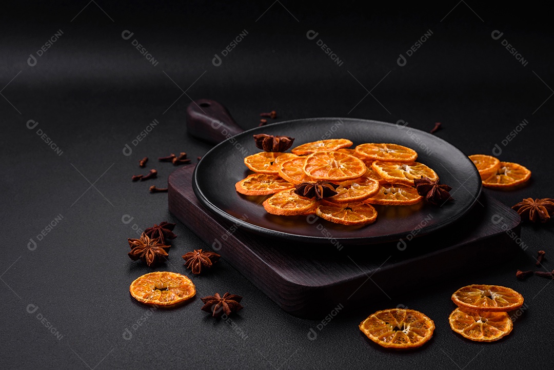 Fatias secas de forma redonda de tangerina de cor laranja brilhante sobre um fundo textural escuro