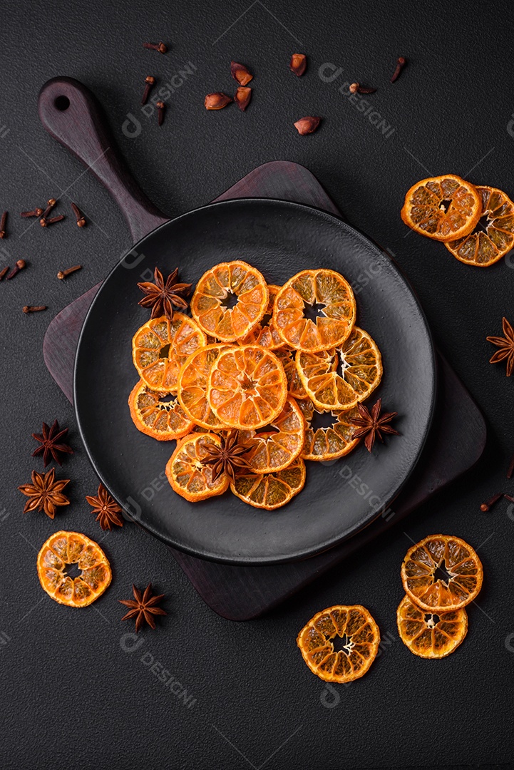Fatias secas de forma redonda de tangerina de cor laranja brilhante sobre um fundo textural escuro
