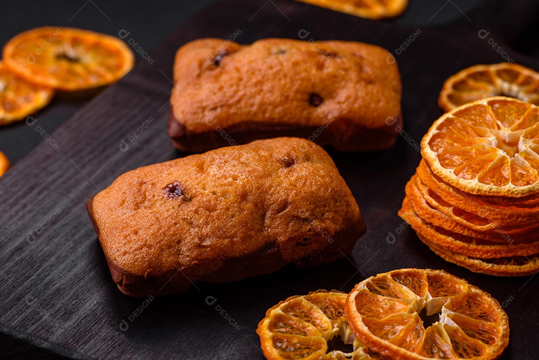 Deliciosos muffins de chocolate e fatias redondas secas de tangerina de cor laranja brilhante sobre um fundo textural escuro