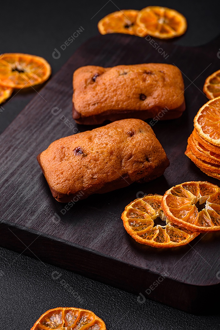 Deliciosos muffins de chocolate e fatias redondas secas de tangerina de cor laranja brilhante sobre um fundo textural escuro
