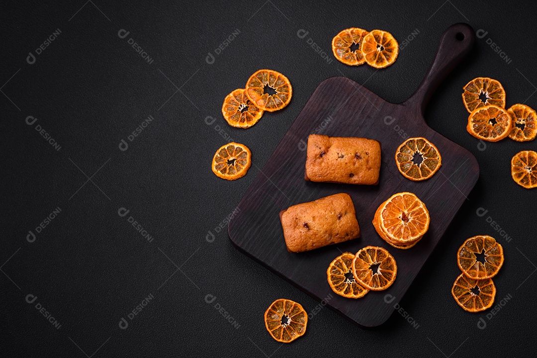 Deliciosos muffins de chocolate e fatias redondas secas de tangerina de cor laranja brilhante sobre um fundo textural escuro