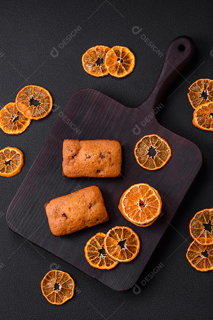 Deliciosos muffins de chocolate e fatias redondas secas de tangerina de cor laranja brilhante sobre um fundo textural escuro