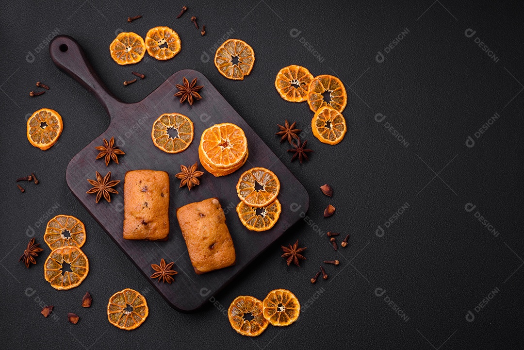 Deliciosos muffins de chocolate e fatias redondas secas de tangerina de cor laranja brilhante sobre um fundo textural escuro