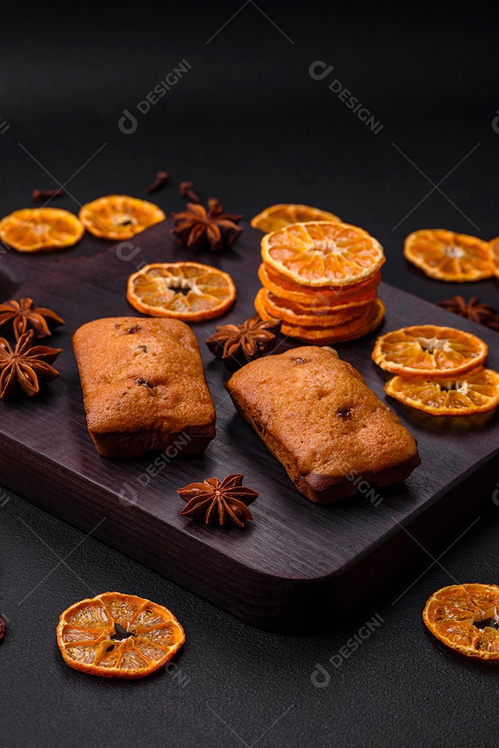 Deliciosos muffins de chocolate e fatias redondas secas de tangerina de cor laranja brilhante sobre um fundo textural escuro