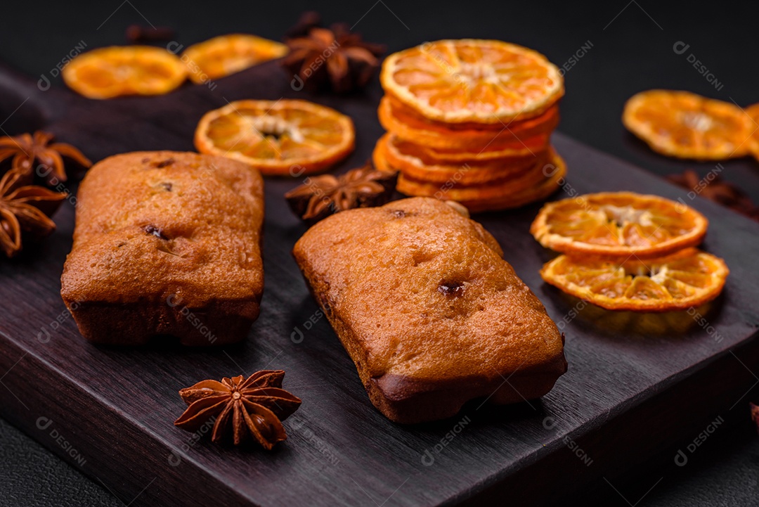 Deliciosos muffins de chocolate e fatias redondas secas de tangerina de cor laranja brilhante sobre um fundo textural escuro