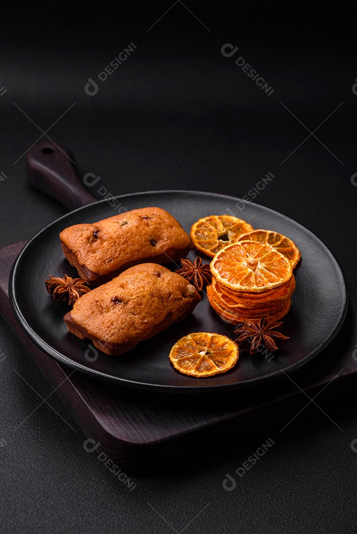 Deliciosos muffins de chocolate e fatias redondas secas de tangerina de cor laranja brilhante sobre um fundo textural escuro