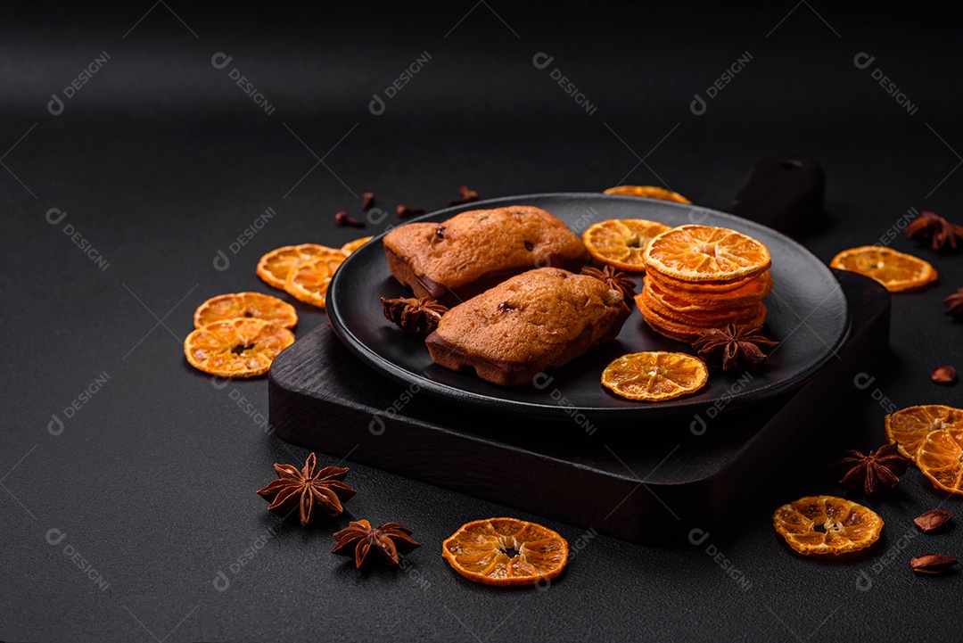 Deliciosos muffins de chocolate e fatias redondas secas de tangerina de cor laranja brilhante sobre um fundo textural escuro