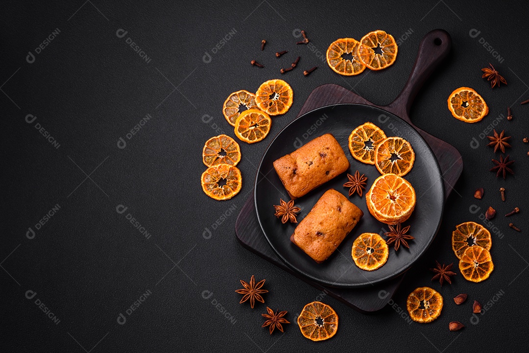 Deliciosos muffins de chocolate e fatias redondas secas de tangerina de cor laranja brilhante sobre um fundo textural escuro