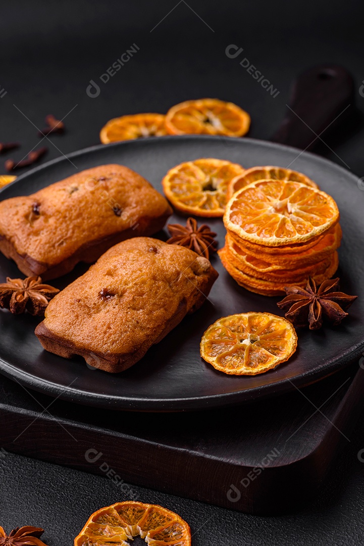 Deliciosos muffins de chocolate e fatias redondas secas de tangerina de cor laranja brilhante sobre um fundo textural escuro