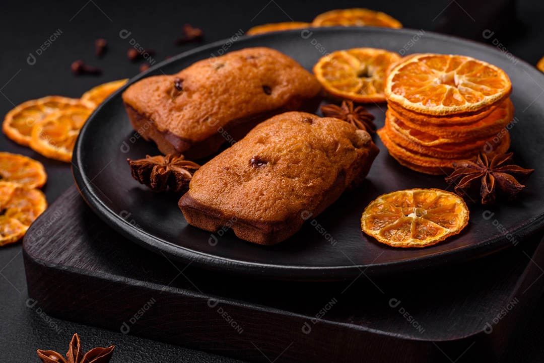 Deliciosos muffins de chocolate e fatias redondas secas de tangerina de cor laranja brilhante sobre um fundo textural escuro