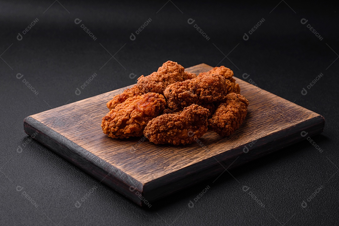 Deliciosas asas de frango empanadas crocantes grelhadas com especiarias e ervas em um fundo escuro de concreto