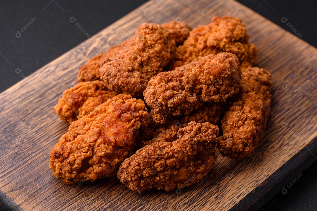 Deliciosas asas de frango empanadas crocantes grelhadas com especiarias e ervas em um fundo escuro de concreto