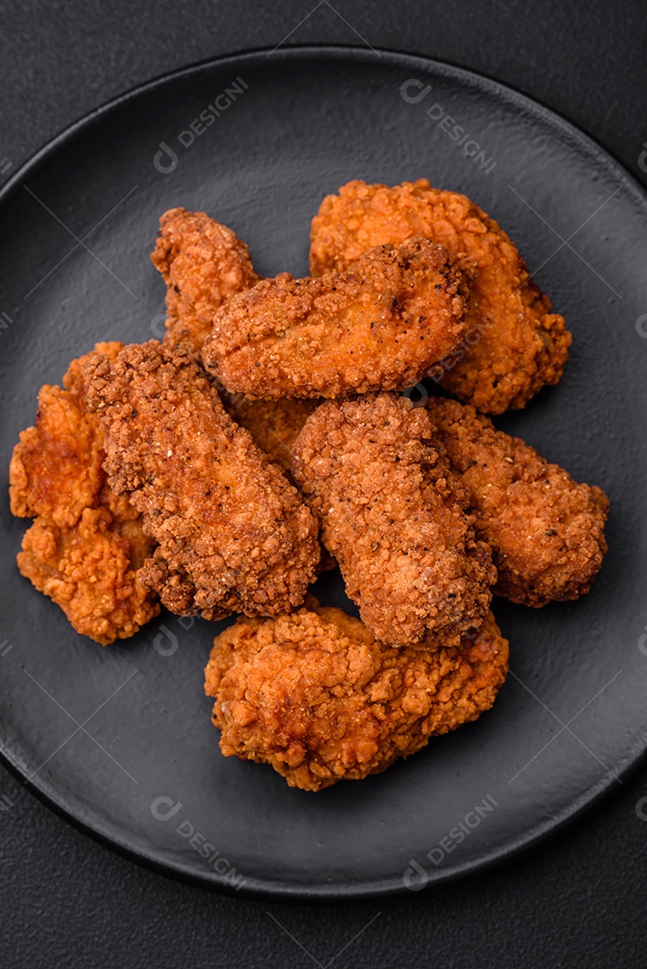 Deliciosas asas de frango empanadas crocantes grelhadas com especiarias e ervas em um fundo escuro de concreto