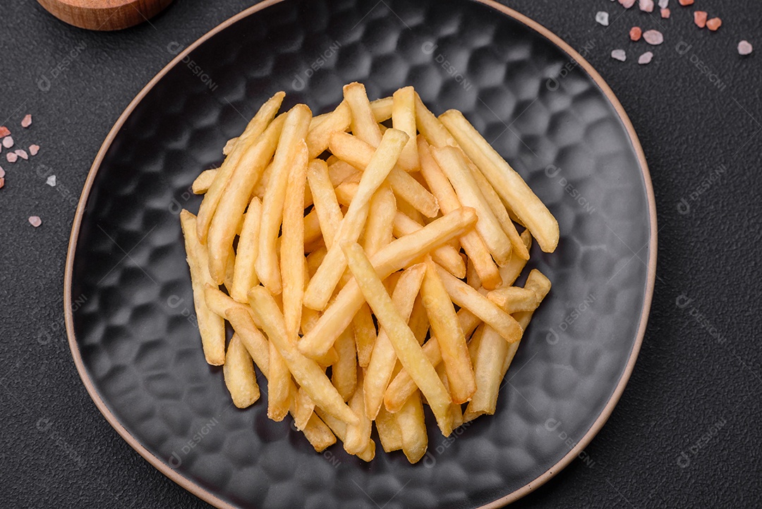 Deliciosas batatas fritas crocantes com sal e especiarias em um fundo escuro de concreto. Alimentos não saudáveis, fast food