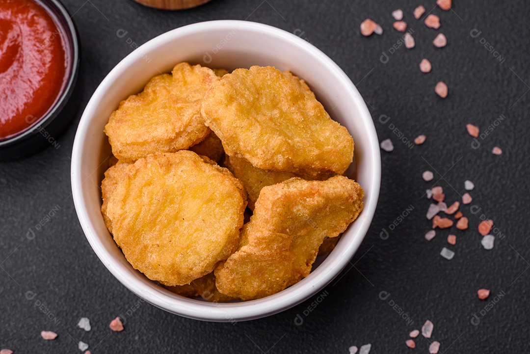 Deliciosos nuggets de frango crocantes com sal e especiarias em um fundo escuro de concreto. Comida lixo, fast-food