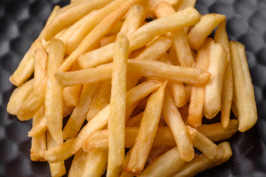 Deliciosas batatas fritas crocantes com sal e especiarias em um fundo escuro de concreto. Alimentos não saudáveis, fast food