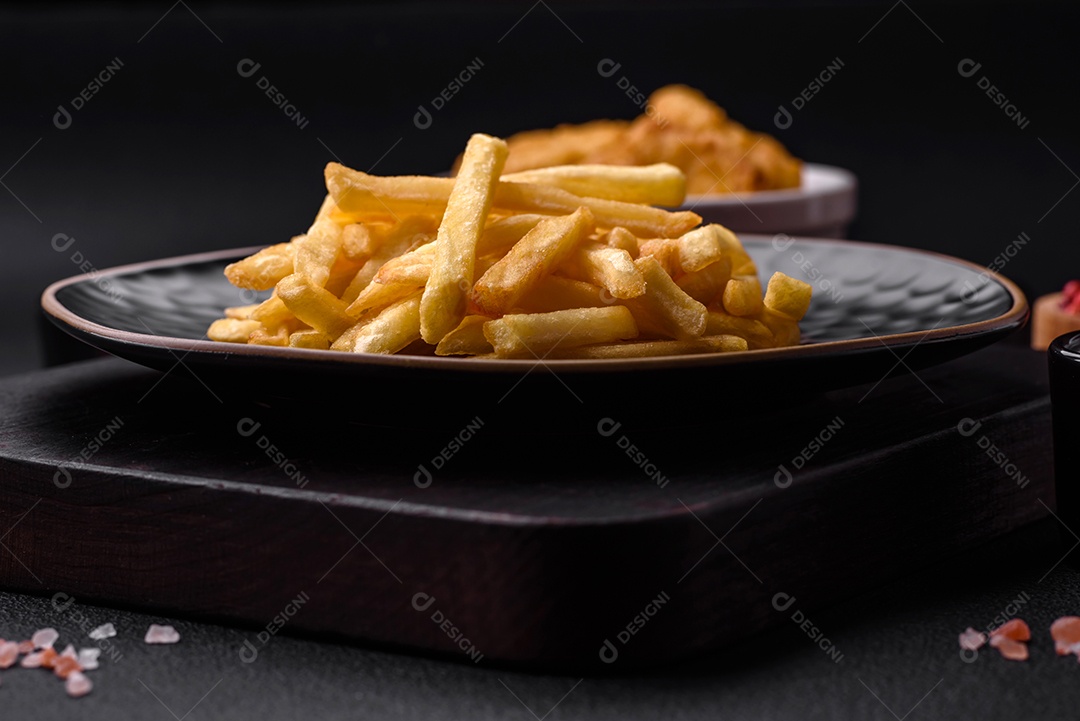 Deliciosas batatas fritas crocantes com sal e especiarias em um fundo escuro de concreto. Alimentos não saudáveis, fast food