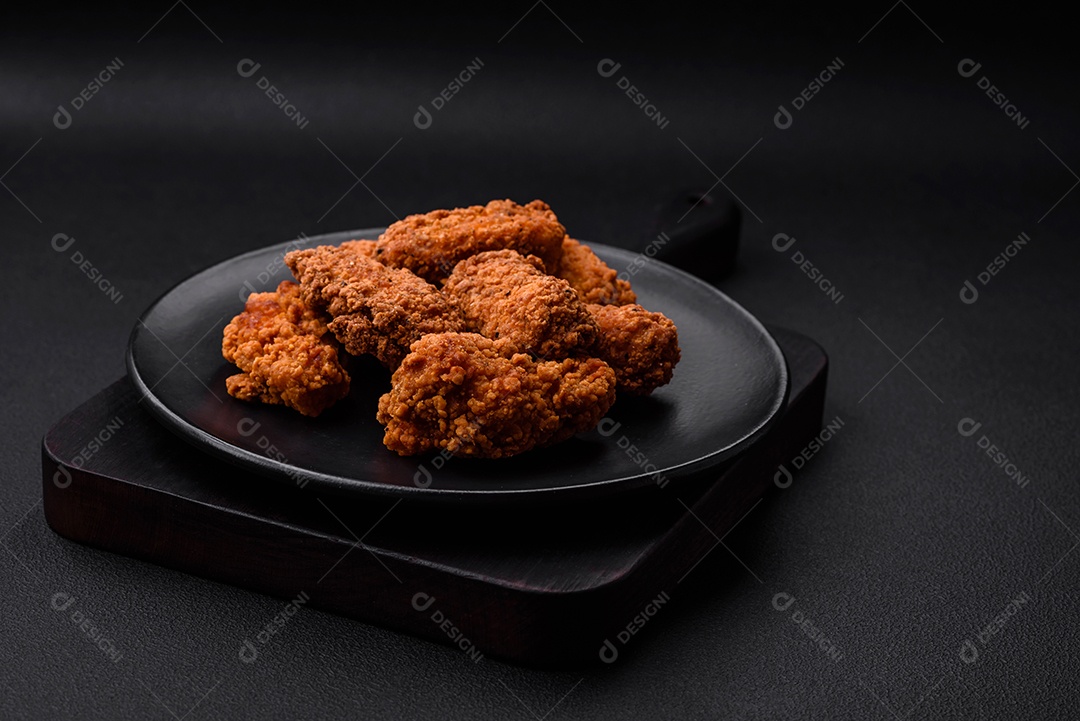 Deliciosas asas de frango empanadas crocantes grelhadas com especiarias e ervas em um fundo escuro de concreto
