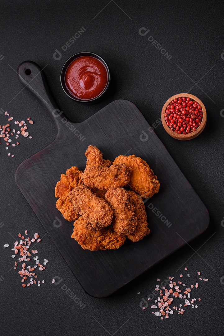 Deliciosas asas de frango empanadas crocantes grelhadas com especiarias e ervas em um fundo escuro de concreto