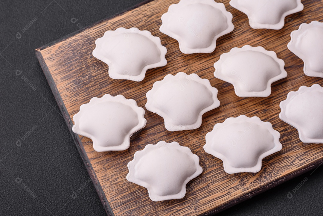 Bolinhos recheados congelados crus em uma tábua de madeira sobre um fundo escuro de concreto