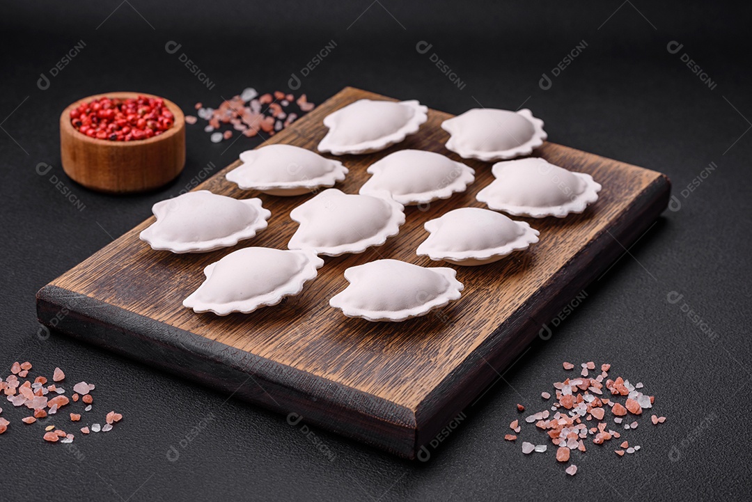 Bolinhos recheados congelados crus em uma tábua de madeira sobre um fundo escuro de concreto