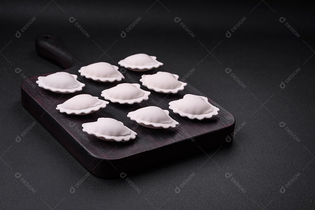 Bolinhos recheados congelados crus em uma tábua de madeira sobre um fundo escuro de concreto