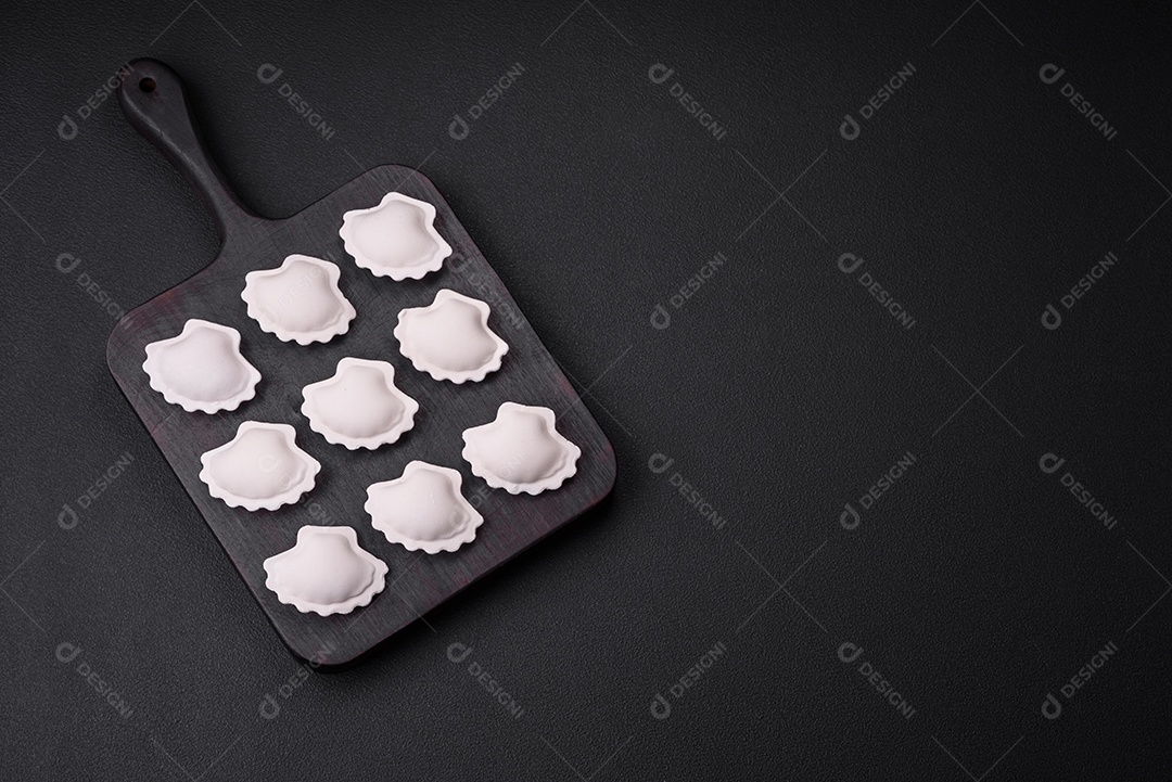 Bolinhos recheados congelados crus em uma tábua de madeira sobre um fundo escuro de concreto