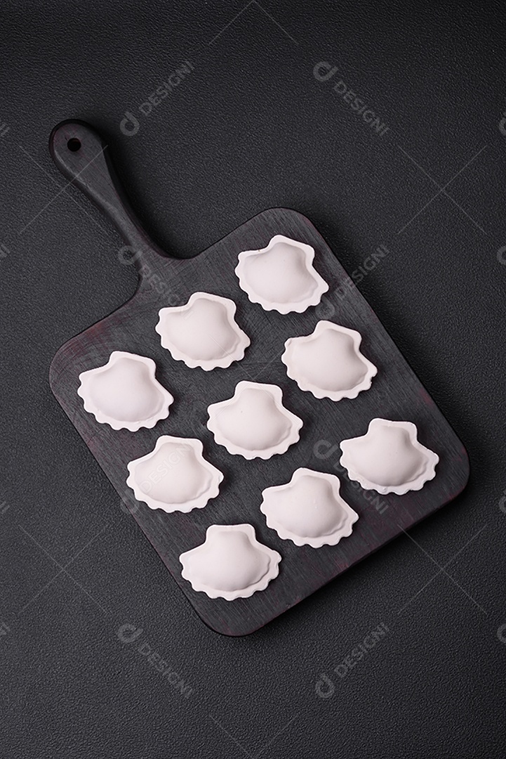 Bolinhos recheados congelados crus em uma tábua de madeira sobre um fundo escuro de concreto