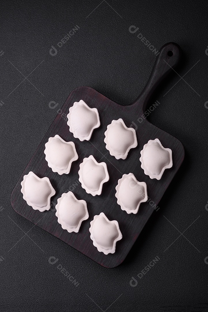 Bolinhos recheados congelados crus em uma tábua de madeira sobre um fundo escuro de concreto