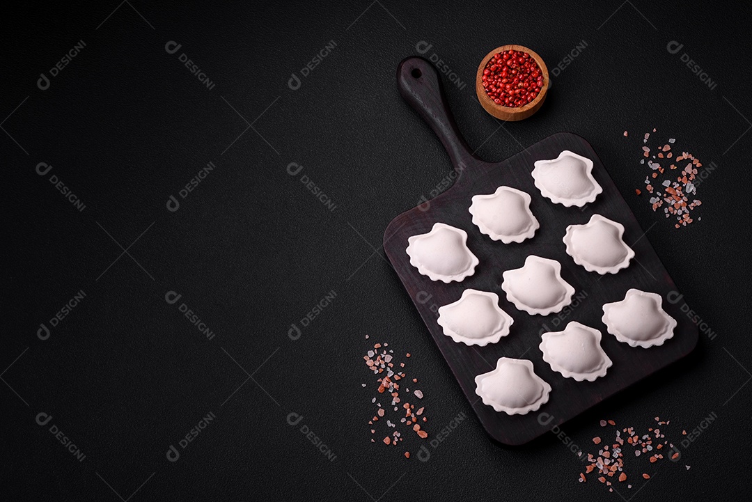 Bolinhos recheados congelados crus em uma tábua de madeira sobre um fundo escuro de concreto