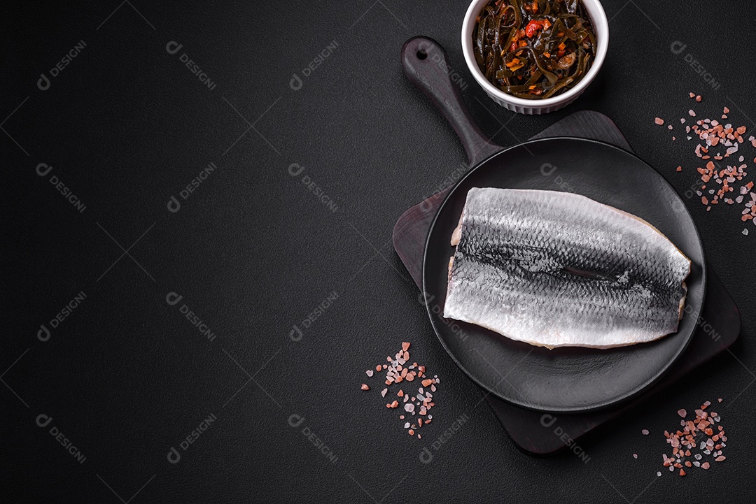 Delicioso filé de arenque salgado em óleo em uma placa de cerâmica preta sobre um fundo escuro de concreto