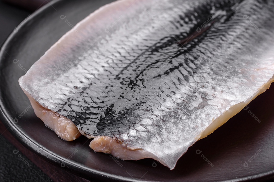 Delicioso filé de arenque salgado em óleo em uma placa de cerâmica preta sobre um fundo escuro de concreto