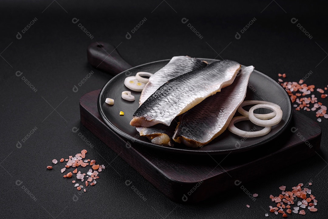 Delicioso filé de arenque salgado em óleo em uma placa de cerâmica preta sobre um fundo escuro de concreto