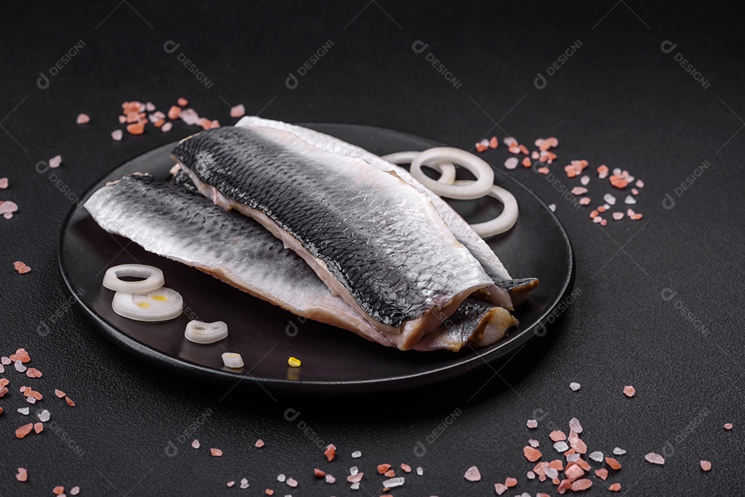 Delicioso filé de arenque salgado em óleo em uma placa de cerâmica preta sobre um fundo escuro de concreto