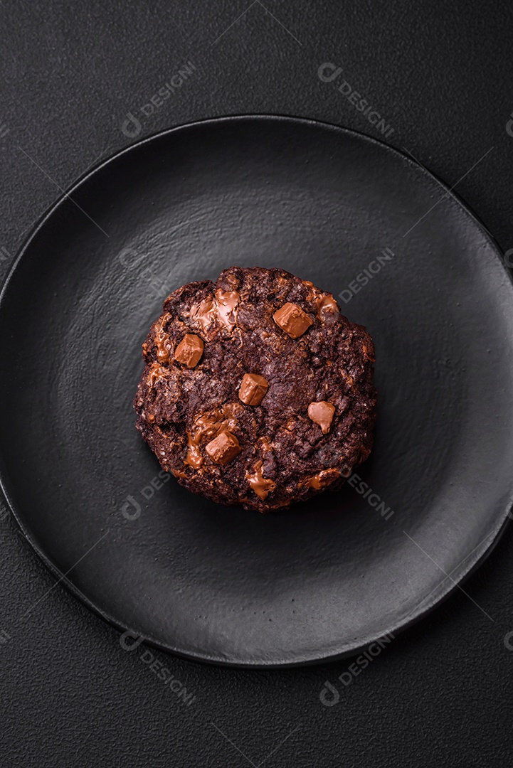 Deliciosos biscoitos redondos de aveia fresca com chocolate em uma placa de cerâmica preta sobre um fundo escuro de concreto