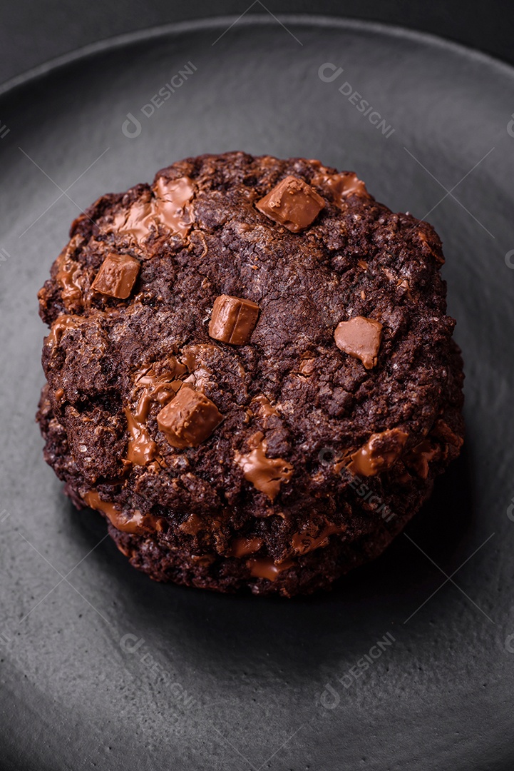 Deliciosos biscoitos redondos de aveia fresca com chocolate em uma placa de cerâmica preta sobre um fundo escuro de concreto
