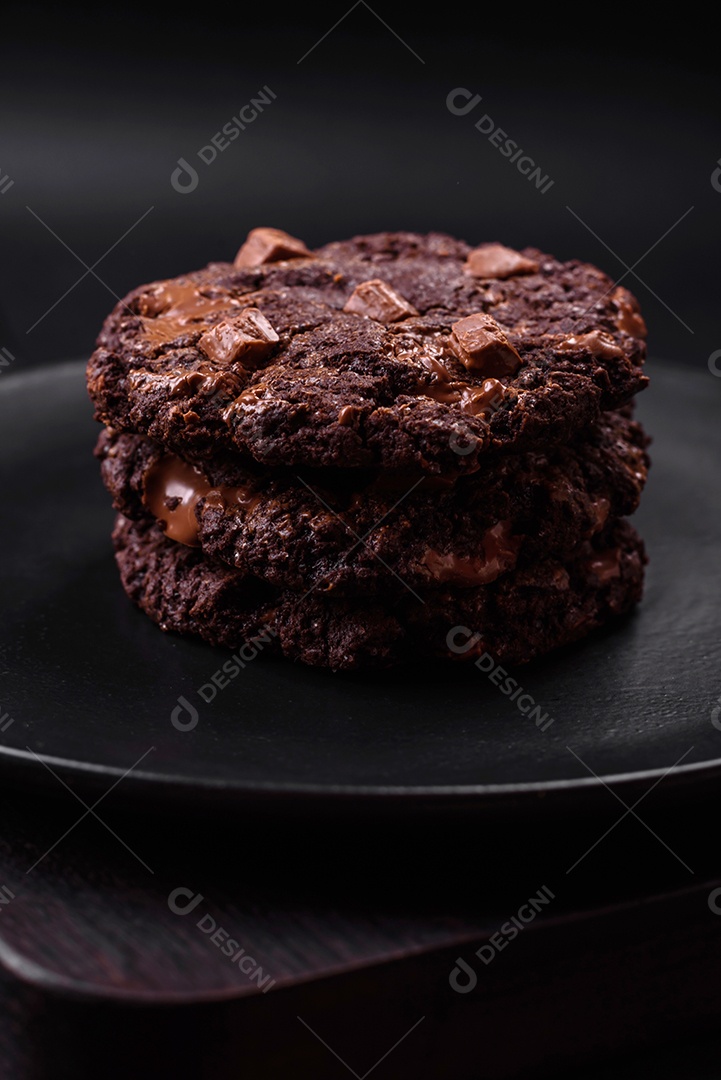 Deliciosos biscoitos redondos de aveia fresca com chocolate em uma placa de cerâmica preta sobre um fundo escuro de concreto