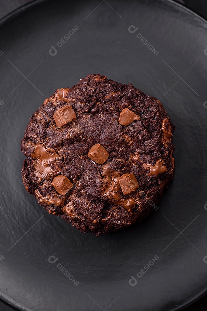 Deliciosos biscoitos redondos de aveia fresca com chocolate em uma placa de cerâmica preta sobre um fundo escuro de concreto
