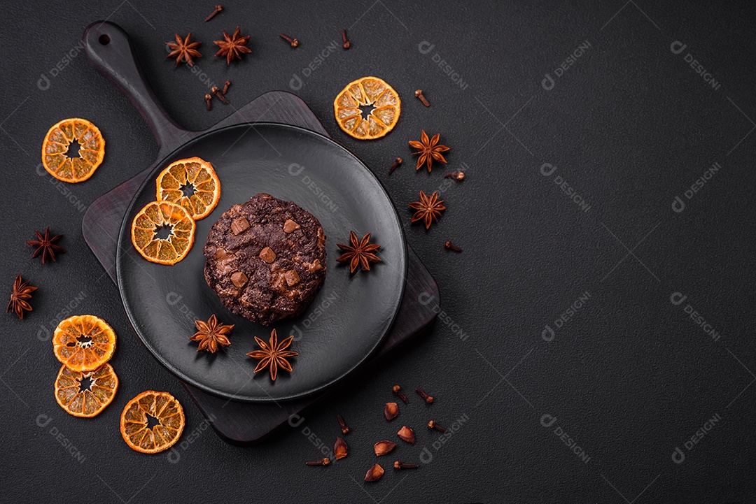 Deliciosos biscoitos redondos de aveia fresca com chocolate em uma placa de cerâmica preta sobre um fundo escuro de concreto