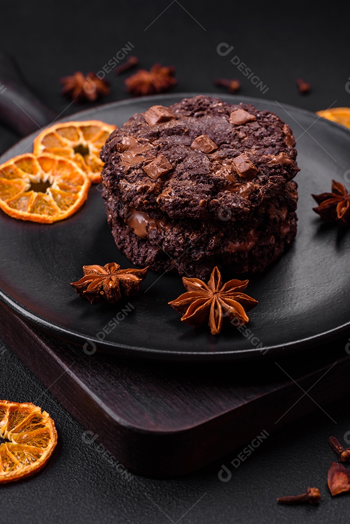 Deliciosos biscoitos redondos de aveia fresca com chocolate em uma placa de cerâmica preta sobre um fundo escuro de concreto