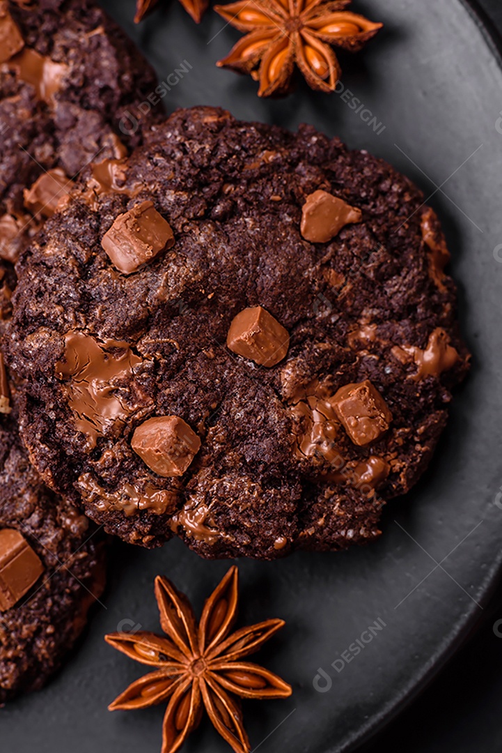 Deliciosos biscoitos redondos de aveia fresca com chocolate em uma placa de cerâmica preta sobre um fundo escuro de concreto