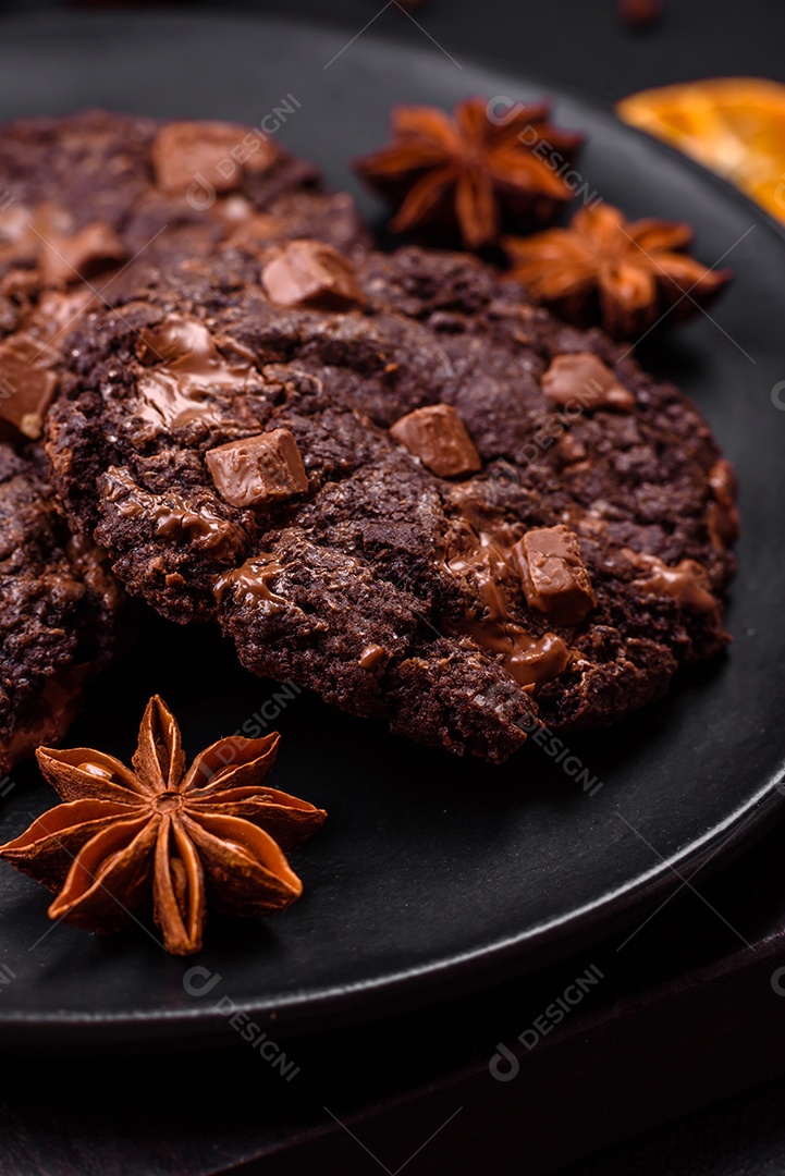 Deliciosos biscoitos redondos de aveia fresca com chocolate em uma placa de cerâmica preta sobre um fundo escuro de concreto