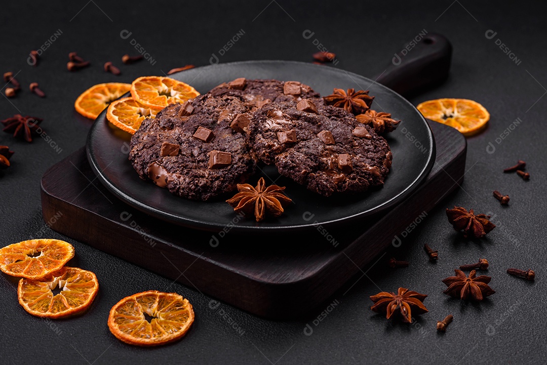 Deliciosos biscoitos redondos de aveia fresca com chocolate em uma placa de cerâmica preta sobre um fundo escuro de concreto