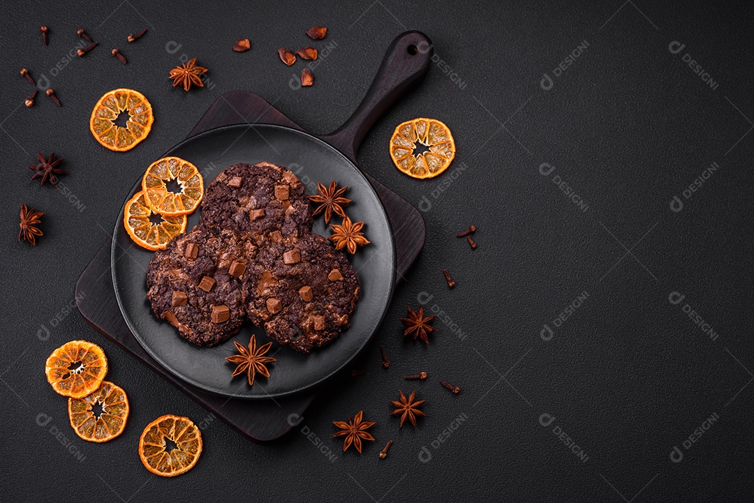 Deliciosos biscoitos redondos de aveia fresca com chocolate em uma placa de cerâmica preta sobre um fundo escuro de concreto