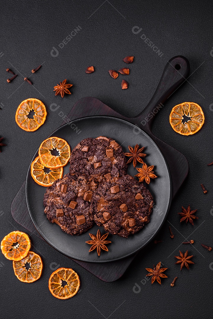 Deliciosos biscoitos redondos de aveia fresca com chocolate em uma placa de cerâmica preta sobre um fundo escuro de concreto