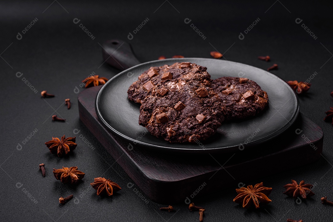 Deliciosos biscoitos redondos de aveia fresca com chocolate em uma placa de cerâmica preta sobre um fundo escuro de concreto