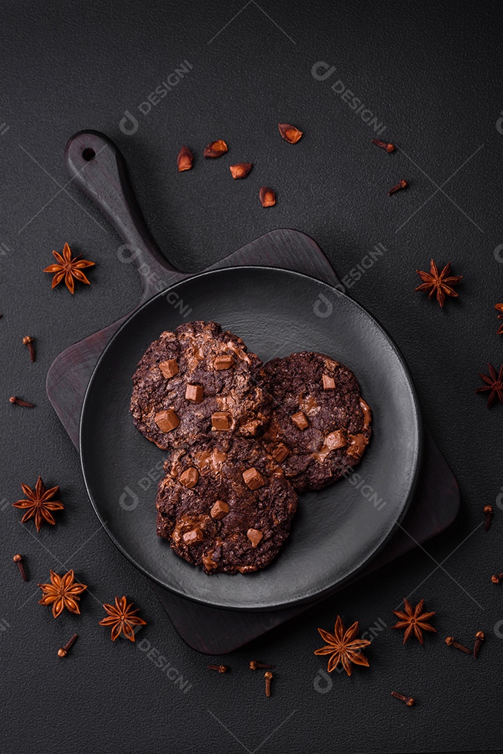 Deliciosos biscoitos redondos de aveia fresca com chocolate em uma placa de cerâmica preta sobre um fundo escuro de concreto