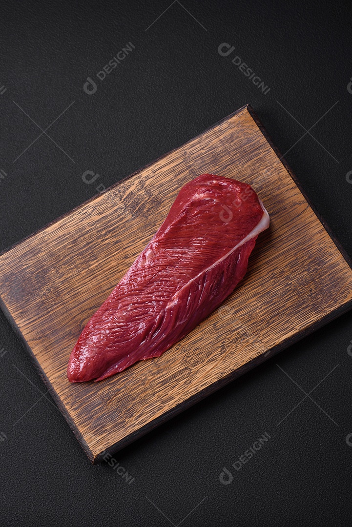 Belo pedaço fresco de carne crua em uma tábua de madeira sobre um fundo escuro de concreto